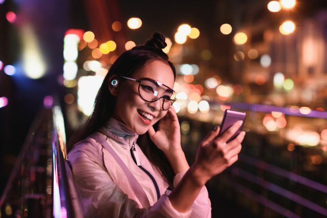 laiminga azijietiška mergina, turinti vaizdo pokalbius naudodama išmanųjį telefoną ir per ausines